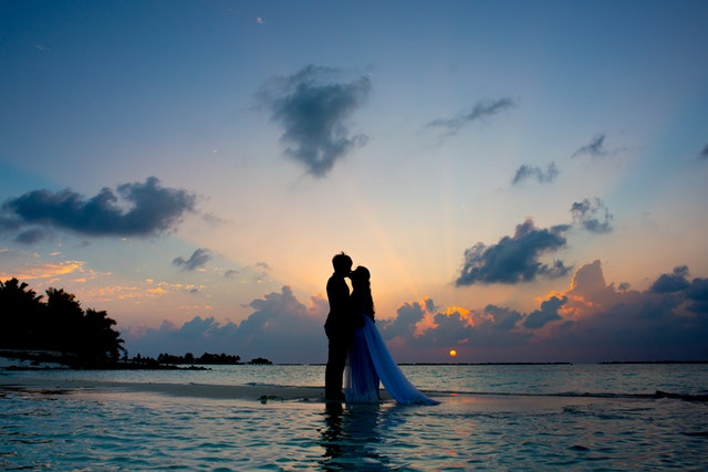 Ženích a nevesta sa bozkávajú pri západe slnka a stoja vo vode.jpg